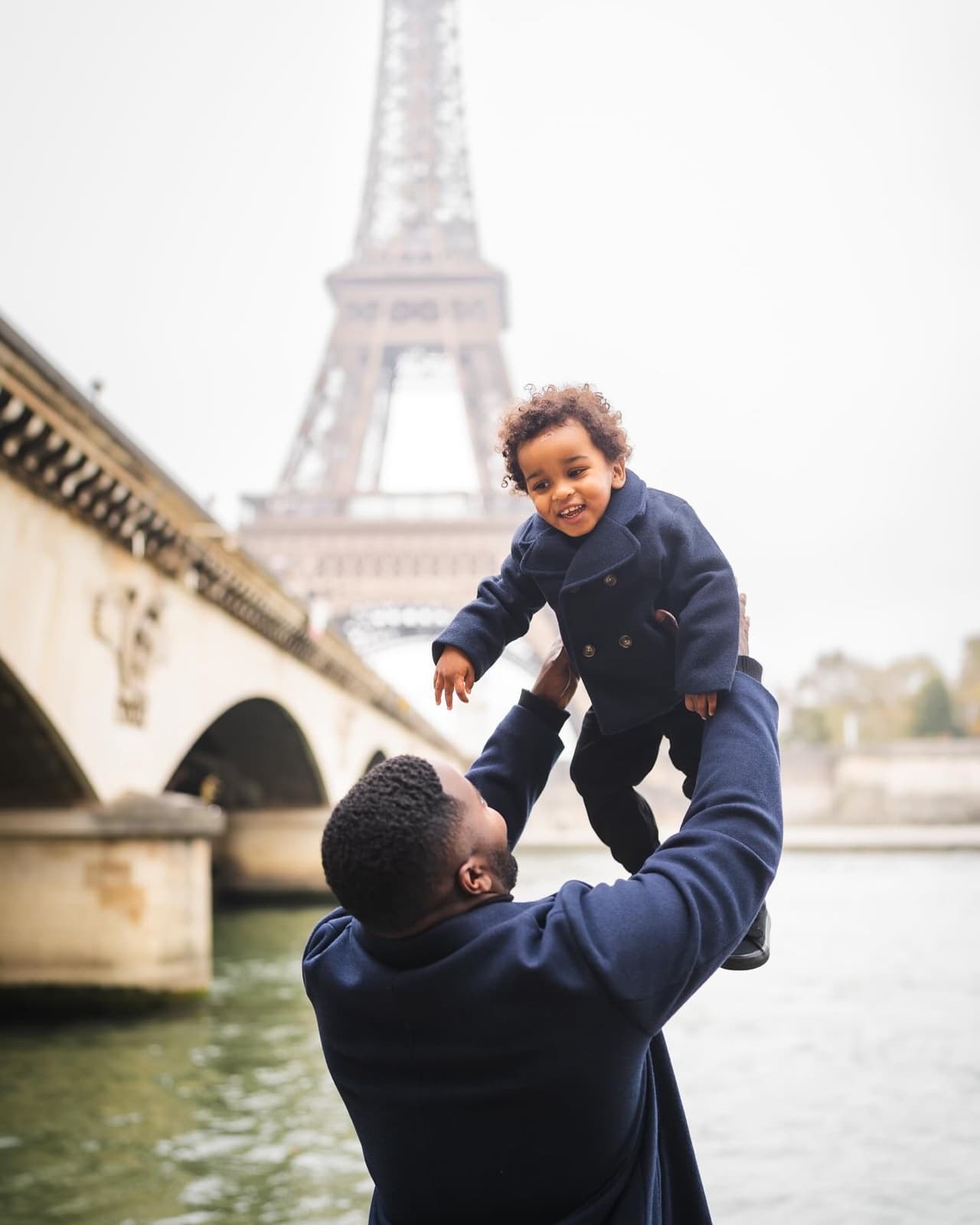 Father lifting his laughing toddler in front of the Eiffel Tower on a Paris family photo session by SabShots