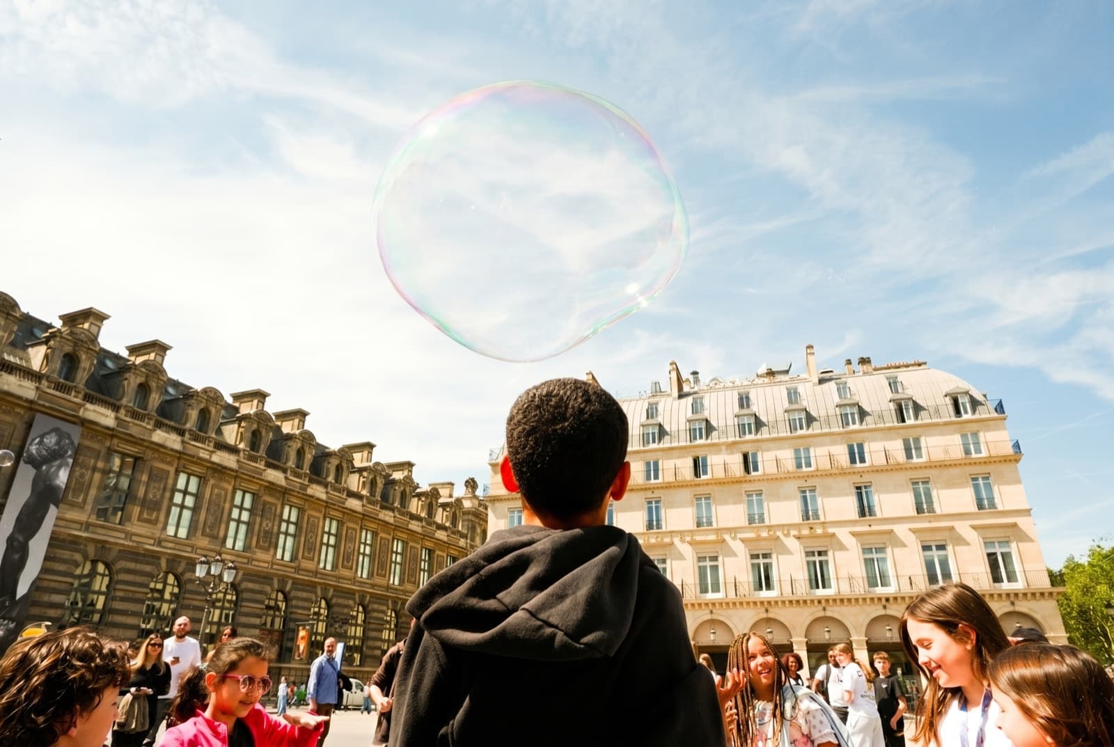 Child watching a giant soap bubble float over the Louvre courtyard in Paris, candid street photography by SabShots