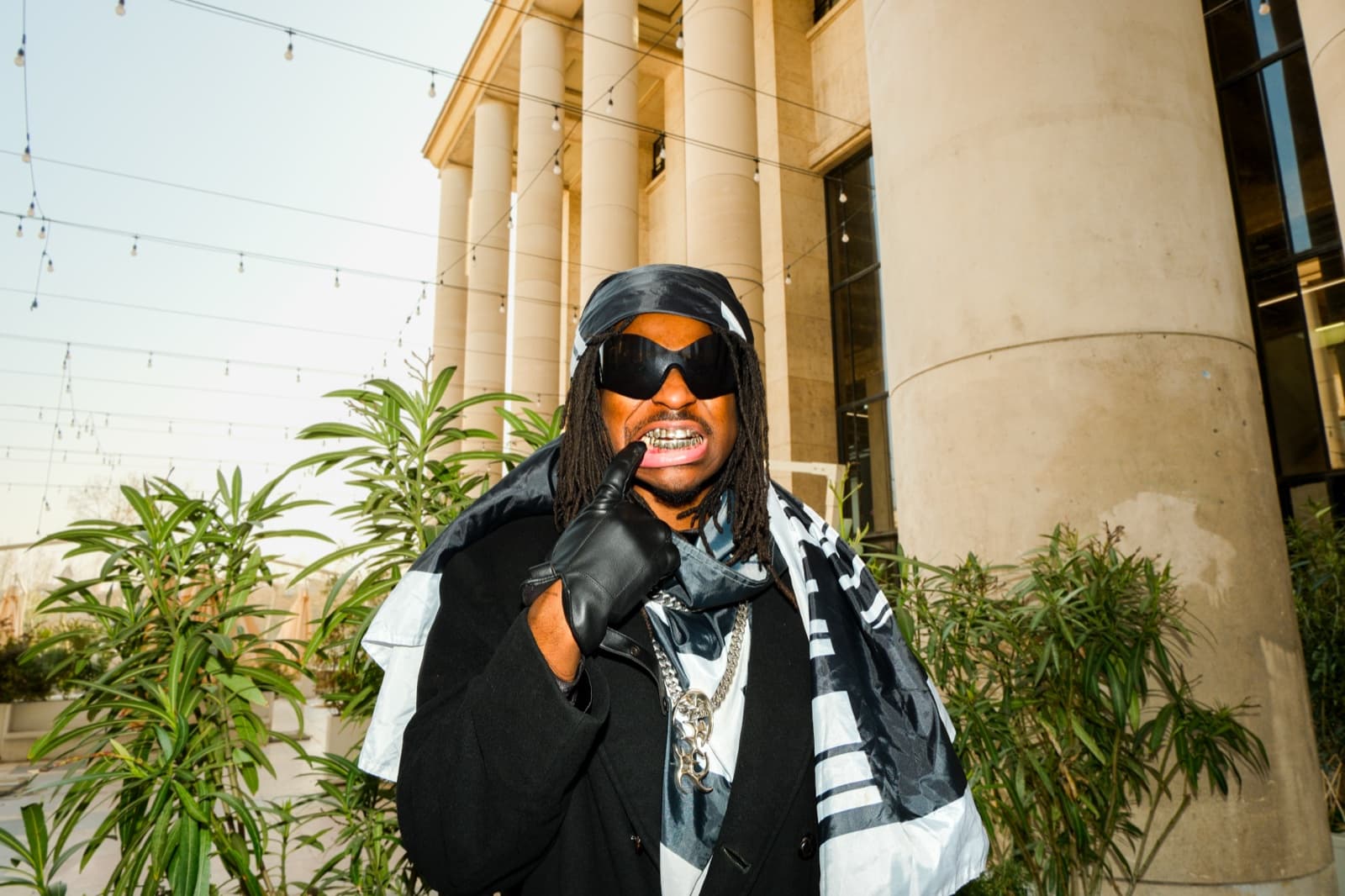 Smiling man in sunglasses and a headscarf posing by a Paris colonnade, candid lifestyle photography by SabShots