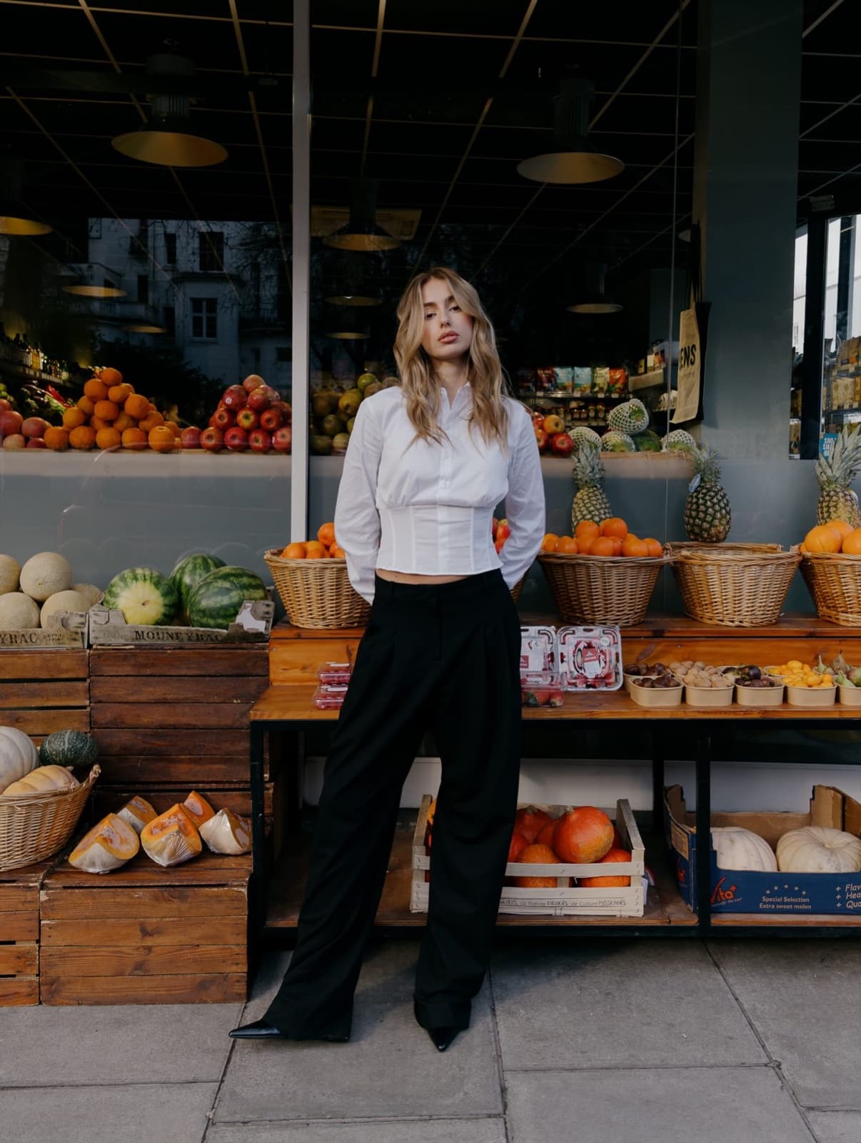 Woman in a white corset top outside a Paris fruit shop, chic lifestyle street photography by SabShots