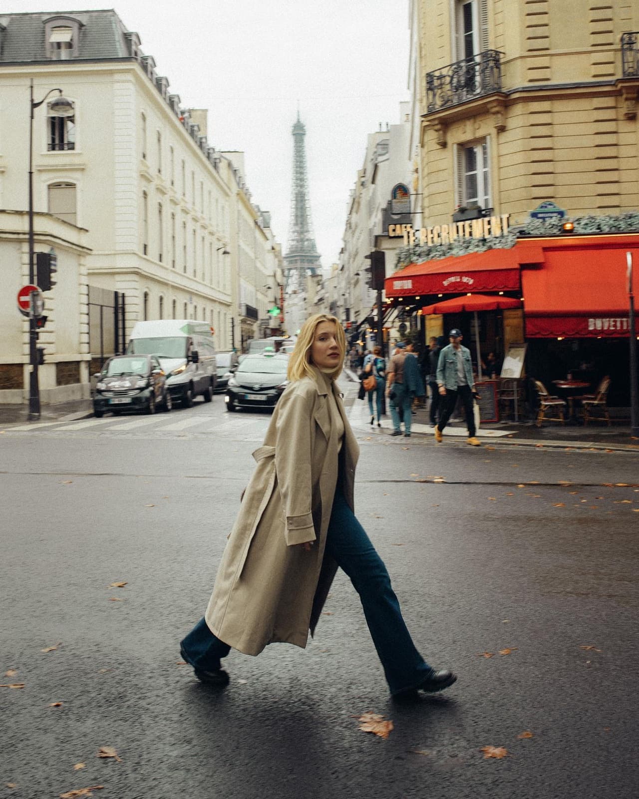 Woman in a trench coat crossing a Paris street with the Eiffel Tower behind, candid lifestyle photography by SabShots