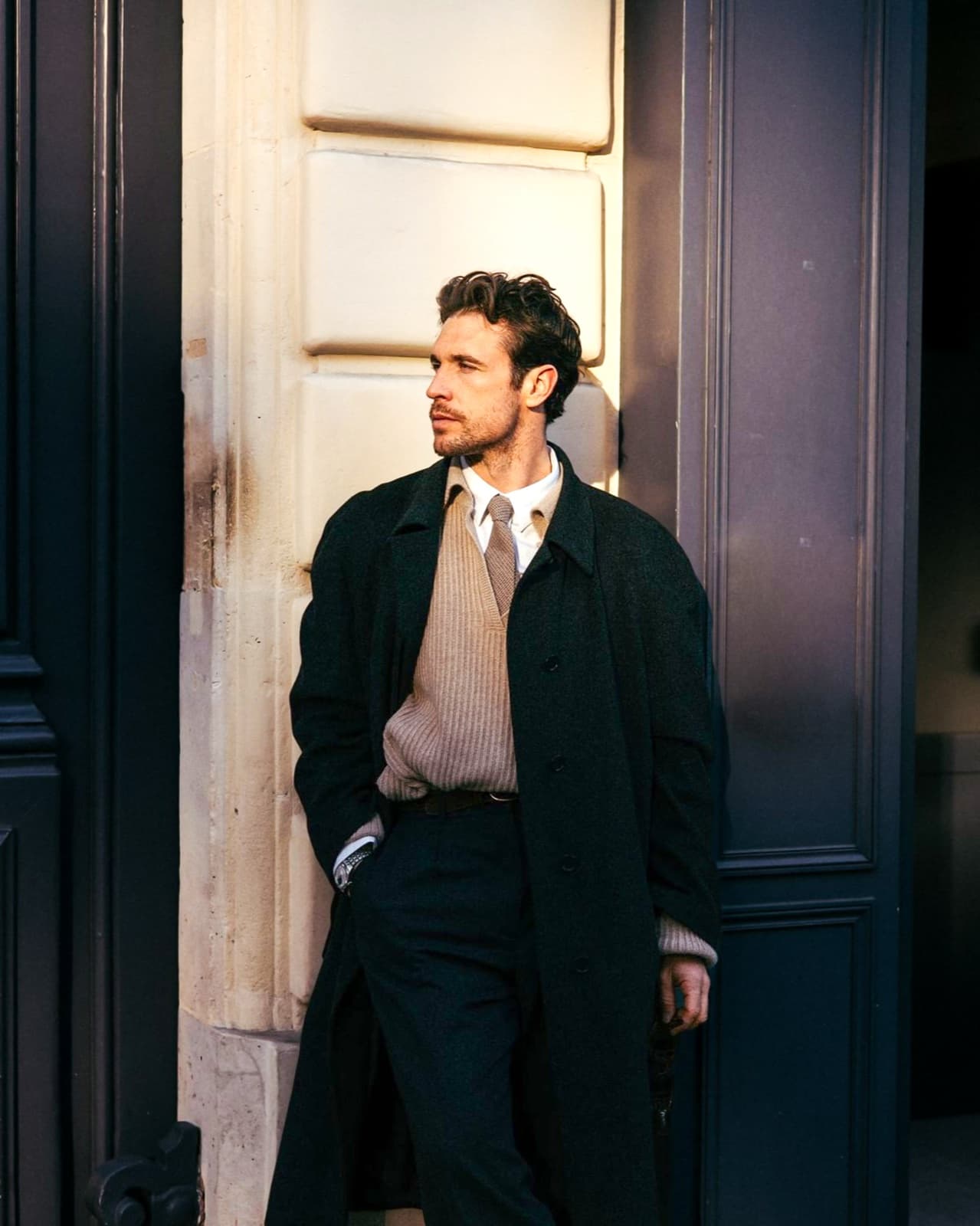 Man in a long overcoat leaning in a doorway in golden Paris light, editorial menswear street photography by SabShots