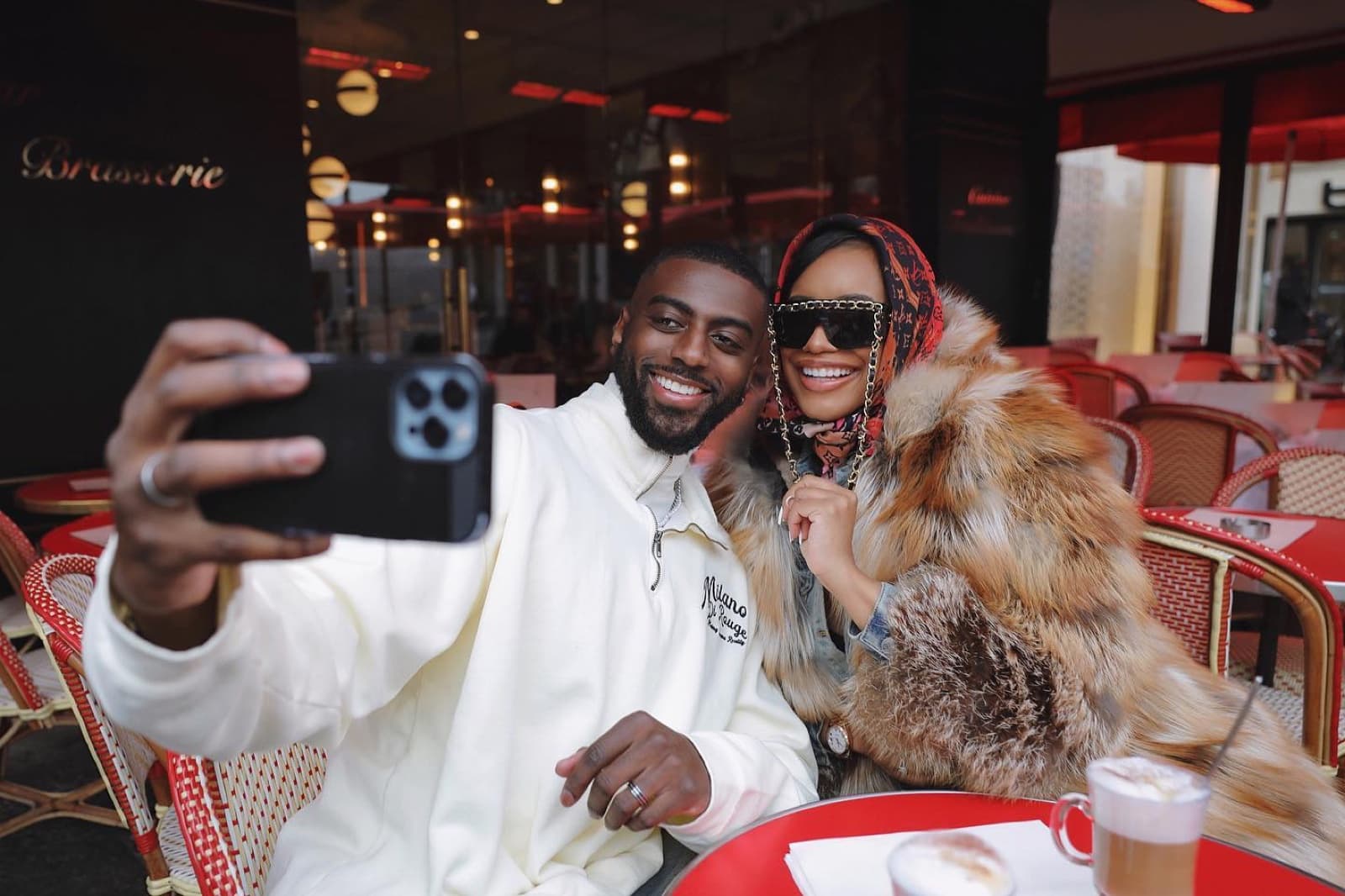 Stylish couple taking a selfie at a classic red Parisian brasserie terrace, a candid couple moment by SabShots