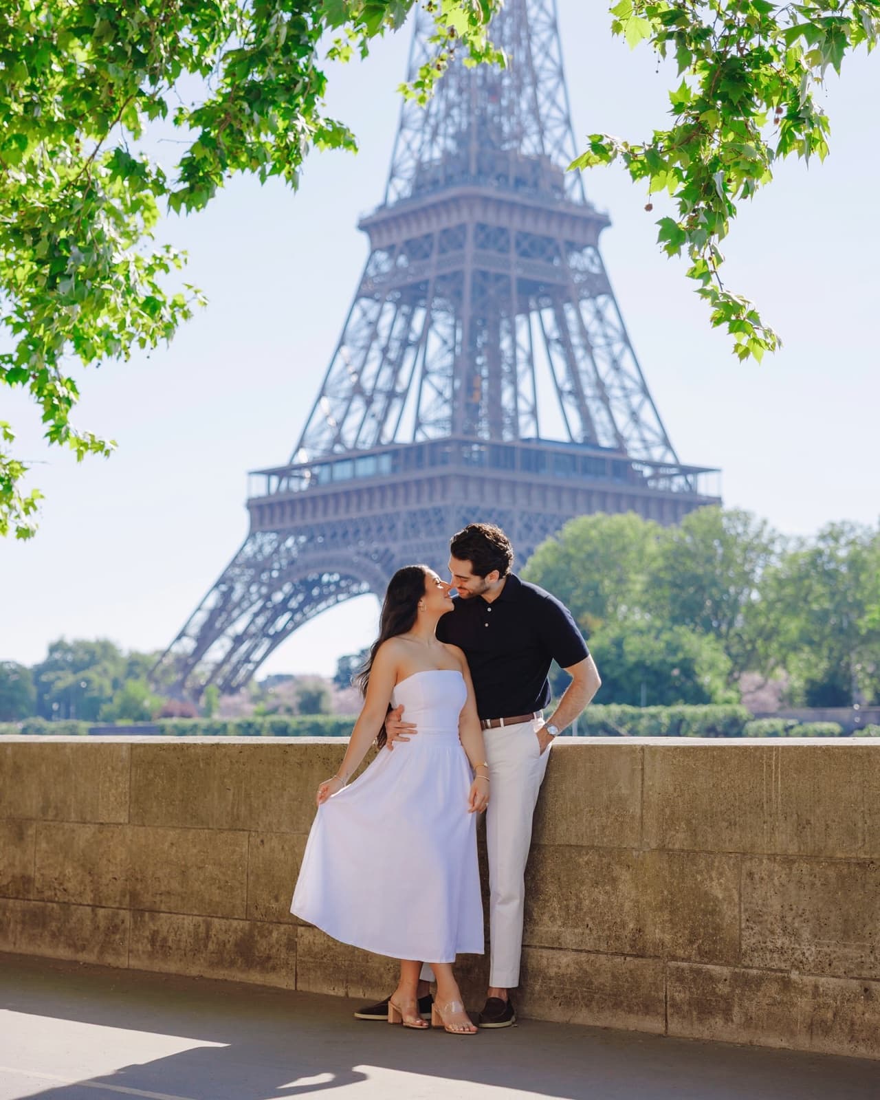 Couple sharing a tender kiss beneath leafy branches framing the Eiffel Tower in Paris by SabShots