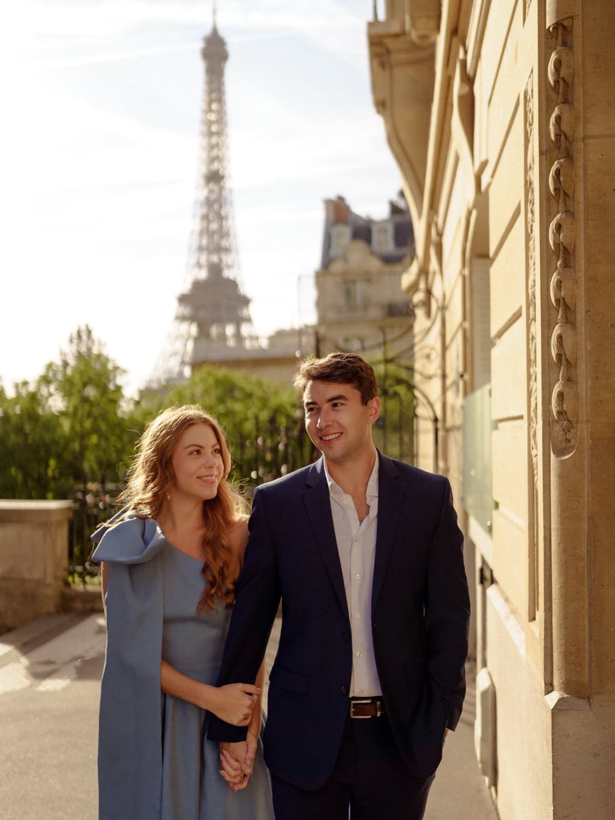 Elegant couple holding hands along a Haussmann avenue with the Eiffel Tower in Paris by SabShots