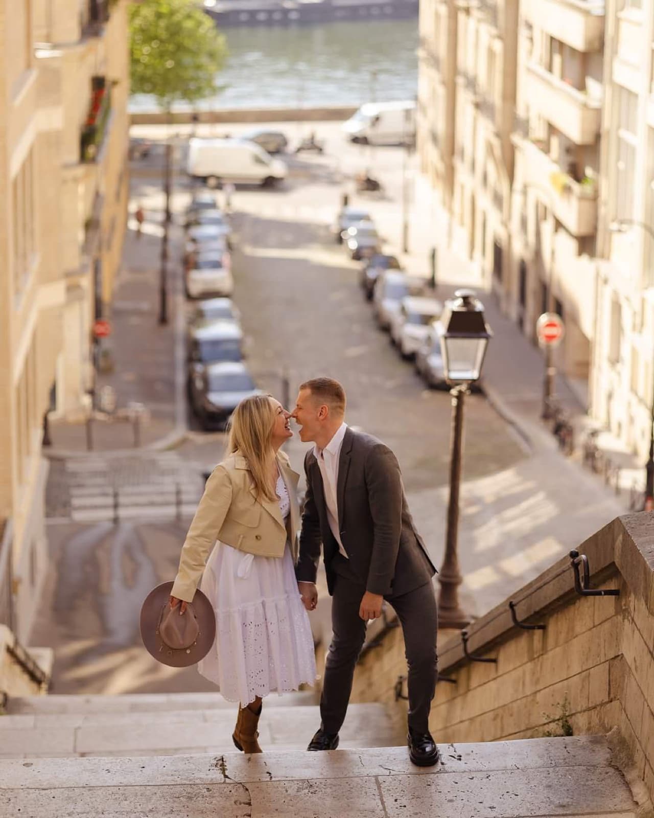 Playful couple touching noses on a stone staircase overlooking the Seine in Paris by SabShots