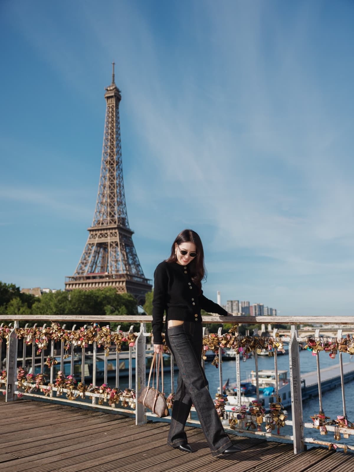 Fashionable woman on the love-lock bridge under blue skies with the Eiffel Tower in Paris by SabShots