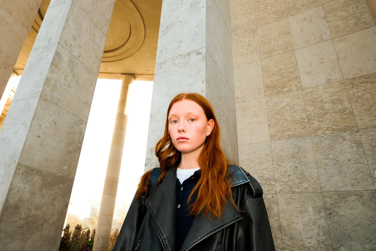 Woman in an oversized leather jacket framed by towering stone columns in Paris, an editorial instagrammable portrait by SabShots