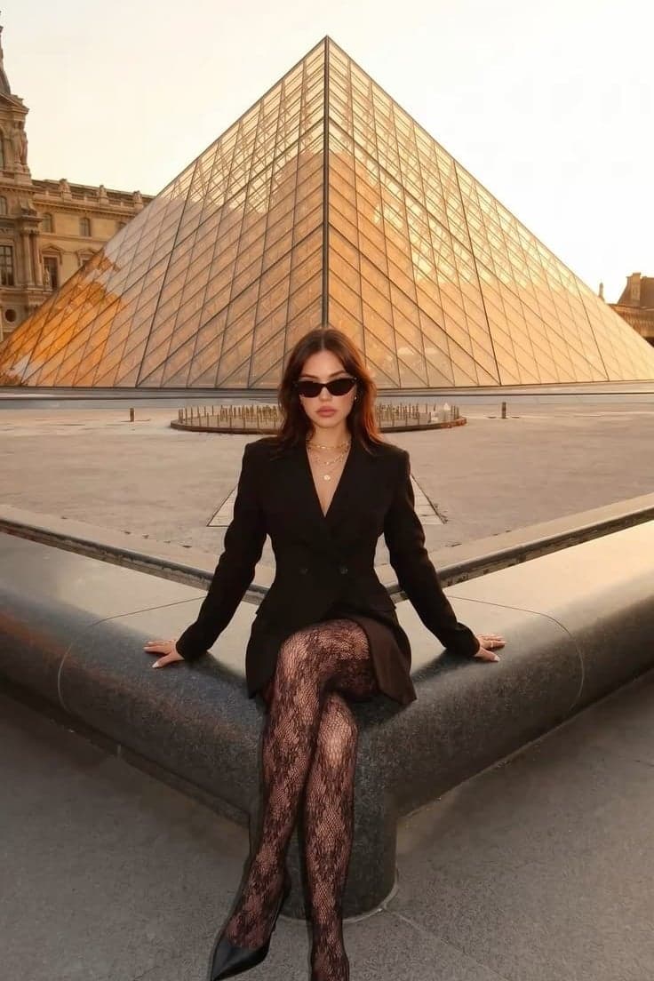 Woman in a black blazer dress seated at the Louvre glass pyramid, Paris lifestyle street portrait by SabShots