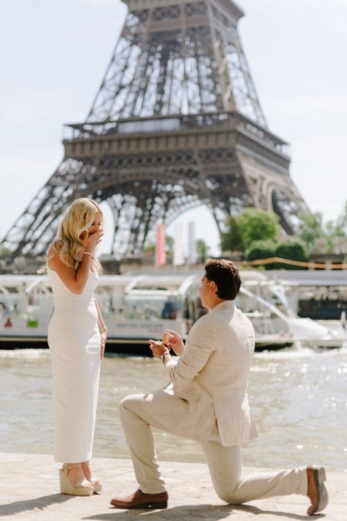 Man in a beige suit kneeling by the Seine below the Eiffel Tower, Paris marriage proposal by SabShots