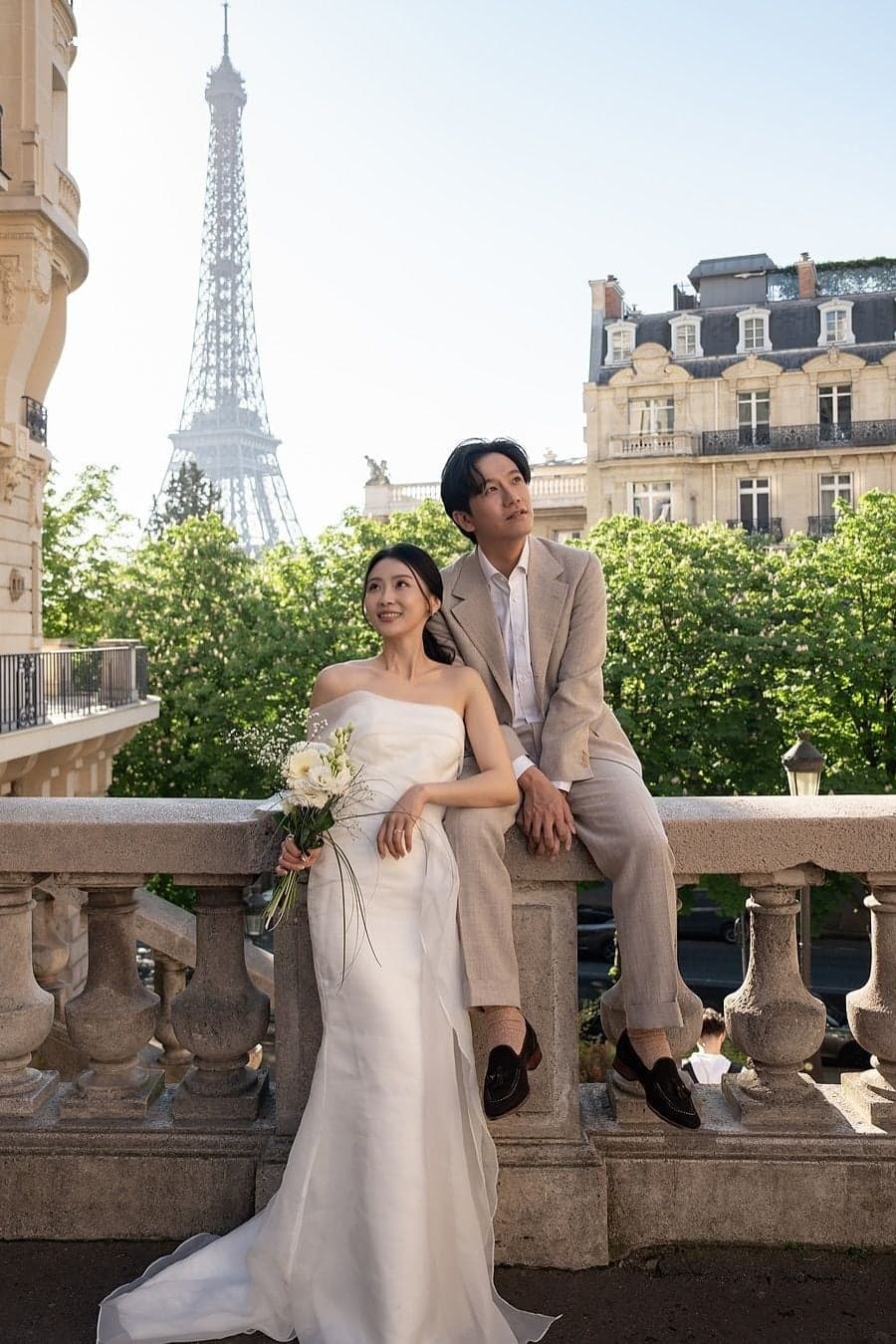 Bride with bouquet and groom in beige suit posing before the Eiffel Tower, Paris wedding photography by SabShots