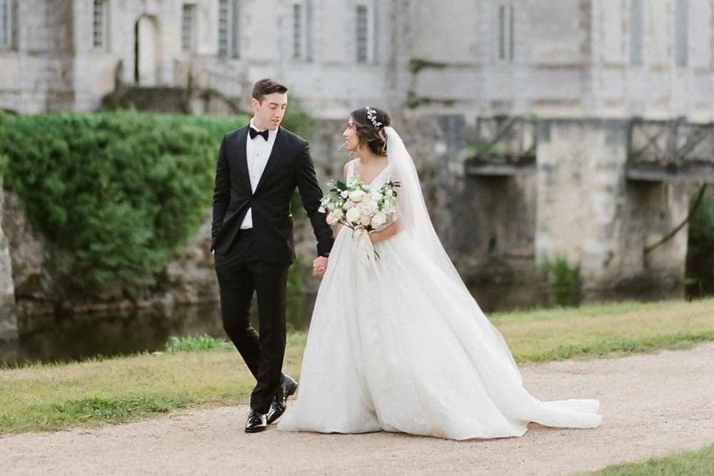 Bride and groom holding hands beside a chateau moat during their Paris wedding by SabShots