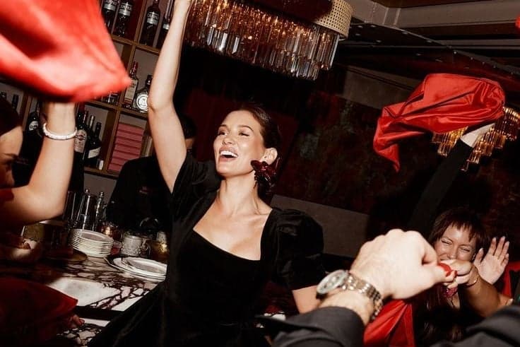 Laughing party guest in black raising her arm amid red napkins at a Paris nightclub event by SabShots