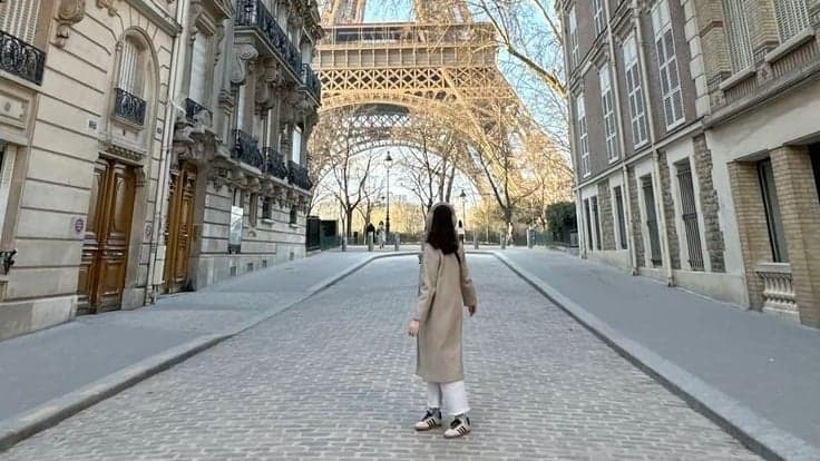 Woman in a beige trench coat walking between Haussmann facades toward the Eiffel Tower in instagrammable Paris by SabShots