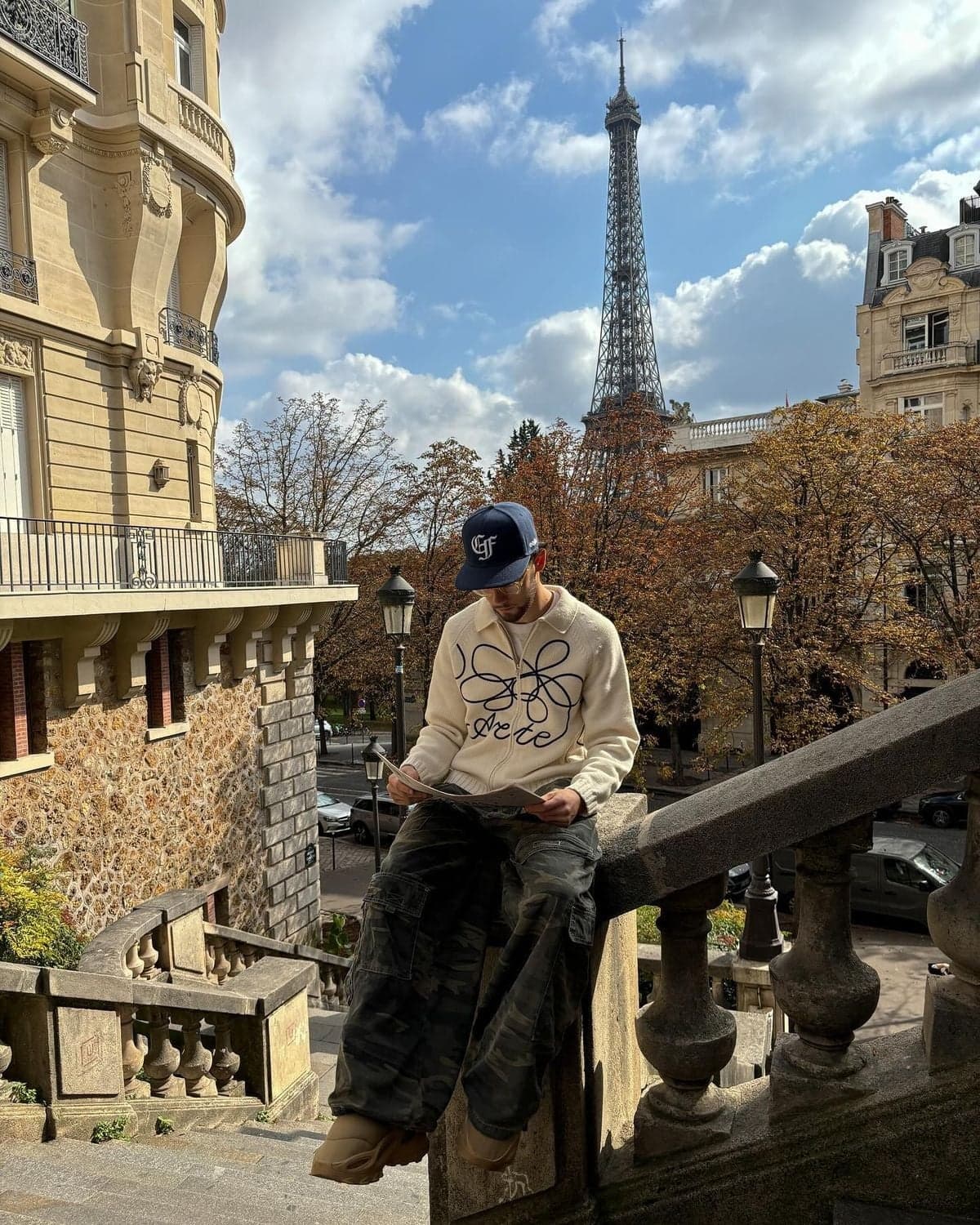 Man in a cream sweater and cap reading on steps, autumn Eiffel Tower photoshoot in Paris by SabShots