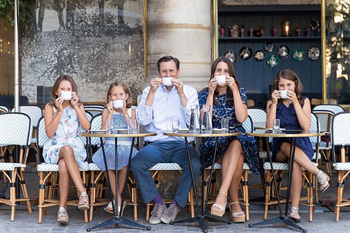 Parents and three daughters sipping coffee at a classic Paris cafe terrace, family photo session by SabShots