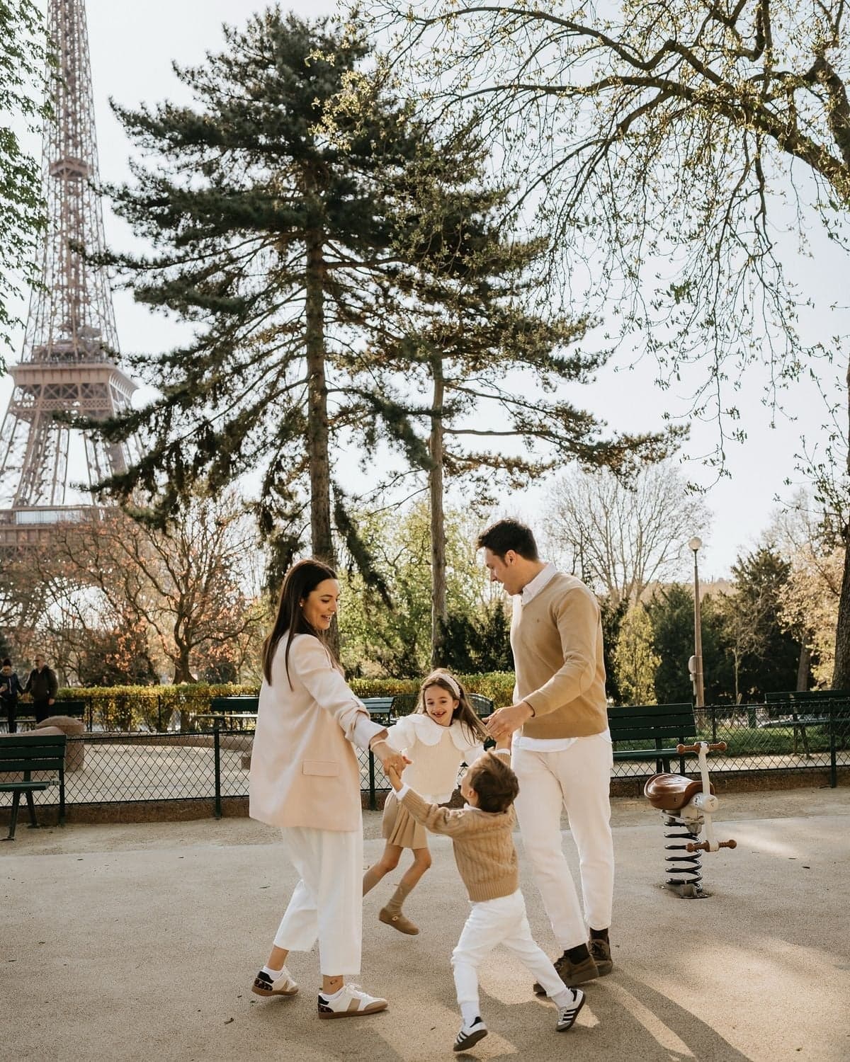 Family dancing in a circle at a playground near the Eiffel Tower, Paris family photo session by SabShots