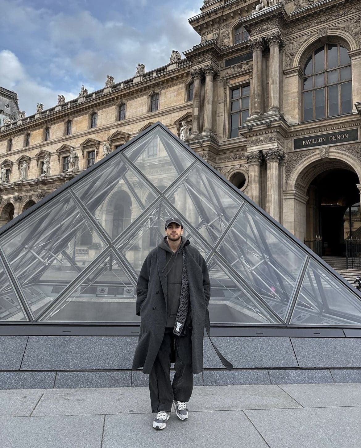 Man in a grey coat and cap before the Louvre Pyramid, an instagrammable Paris photo spot by SabShots