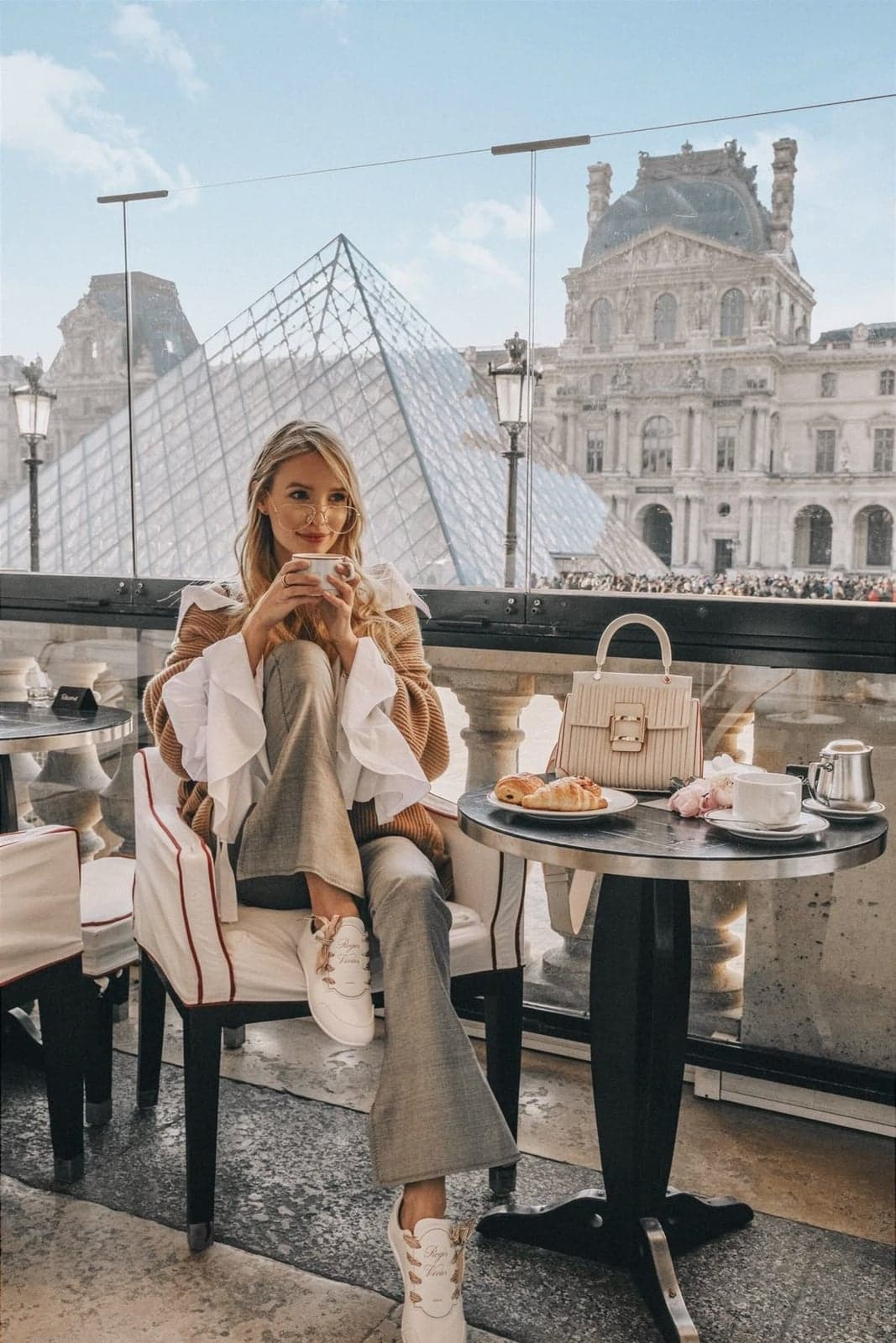 Woman sipping coffee at a cafe terrace overlooking the Louvre Pyramid, an aesthetic instagrammable Paris moment by SabShots