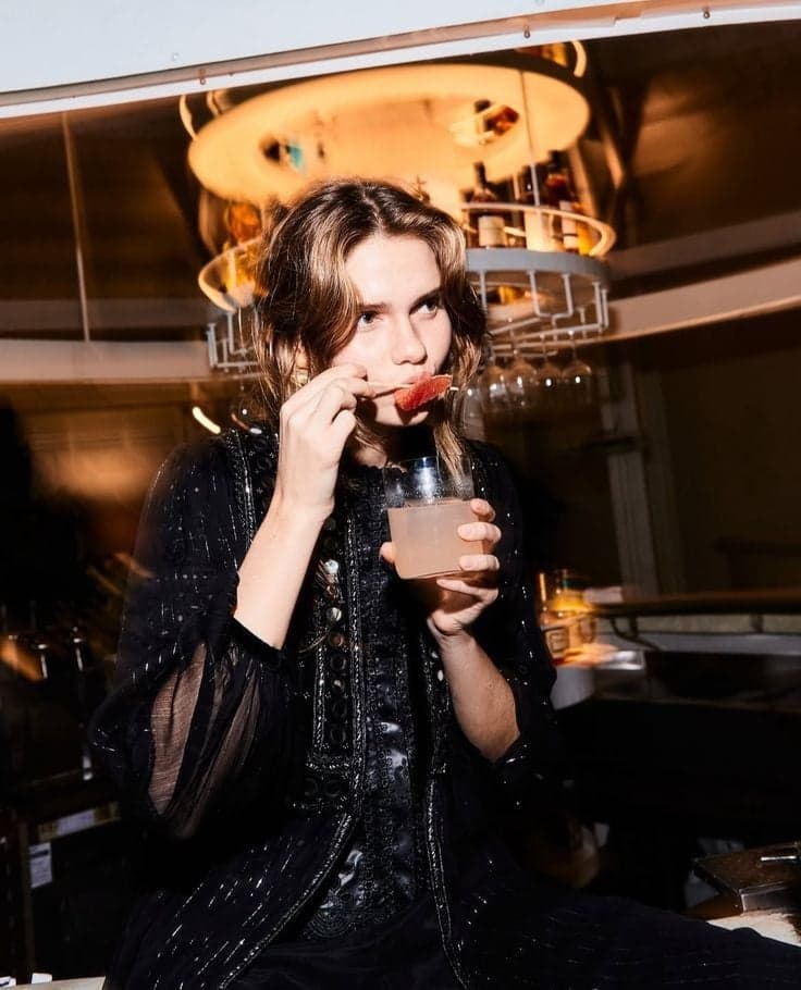 Guest in sheer black blouse sipping a pink cocktail under warm light at a Paris club by SabShots