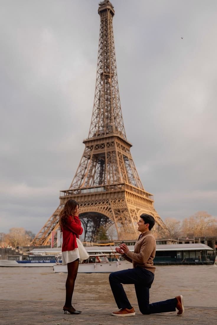 Man kneeling as his girlfriend in red reacts beneath the Eiffel Tower, a winter Paris proposal by SabShots