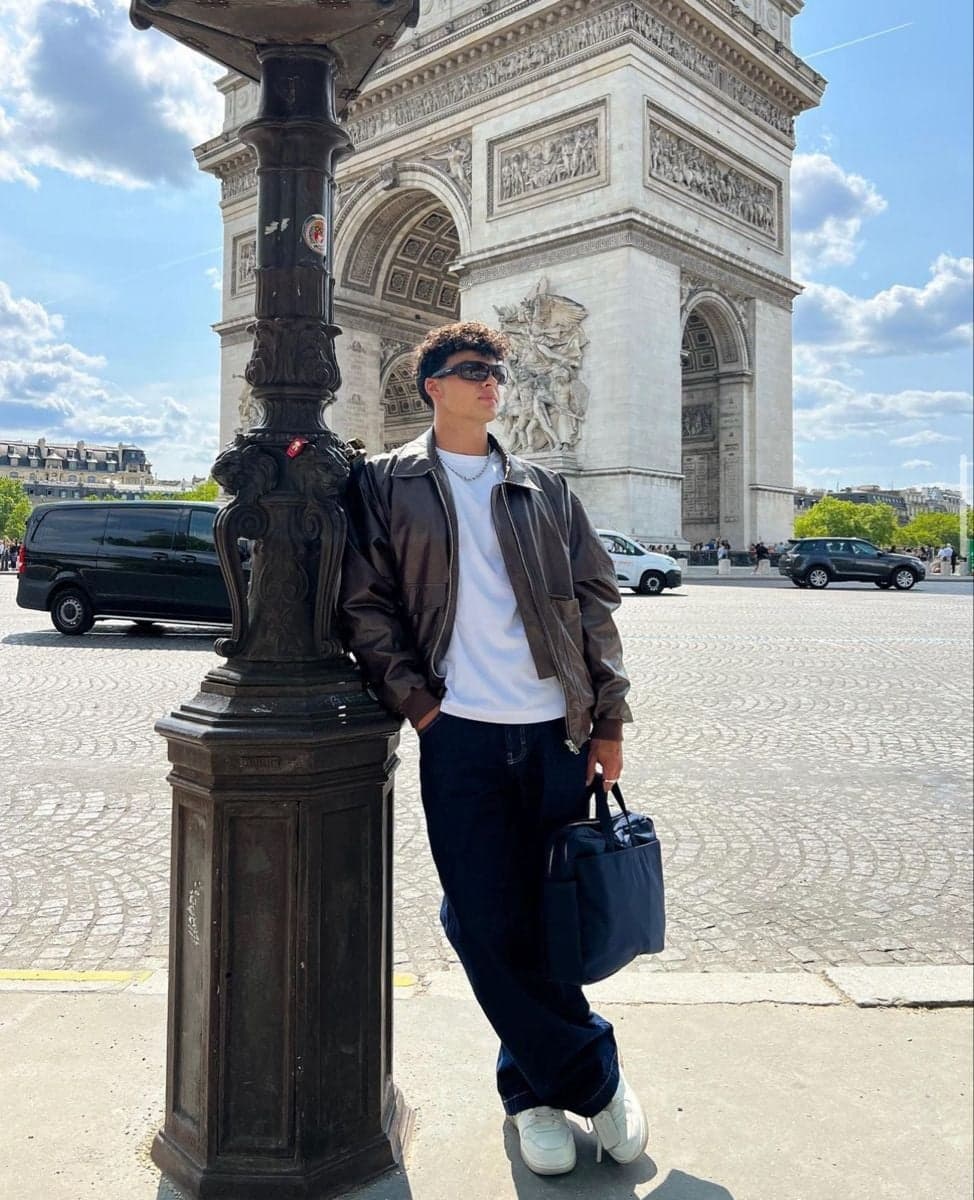Man in a brown leather jacket posing at the Arc de Triomphe, Paris street style photography by SabShots