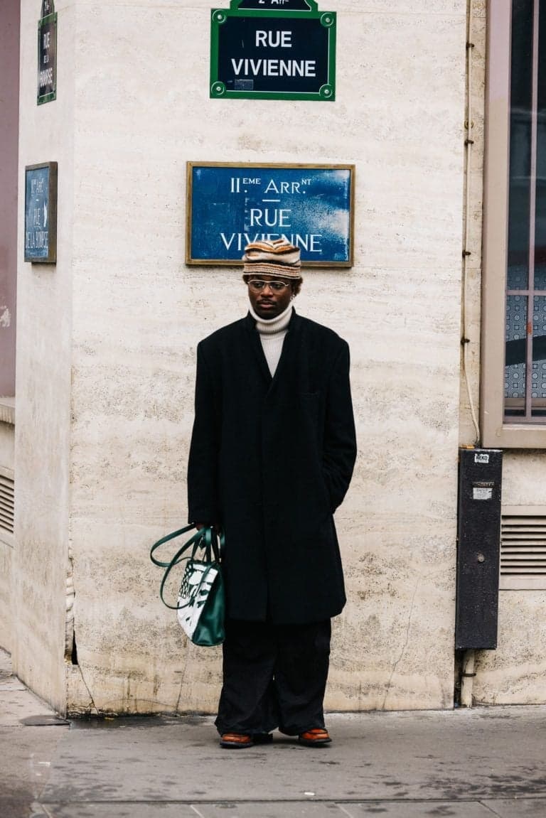 Man in a long black coat and beige headwrap on Rue Vivienne, Paris street style portrait by SabShots