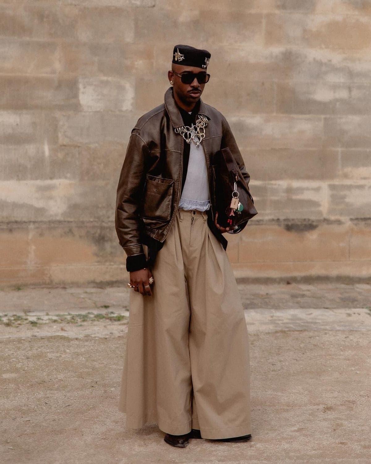 Man in a black cap and wide-leg beige trousers against a Paris wall, editorial street portrait by SabShots