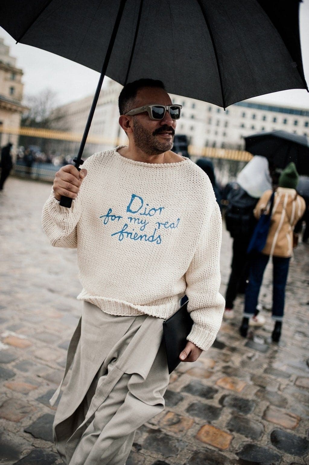 Man with a black umbrella in a cream Dior sweater on Paris cobblestones, lifestyle street photography by SabShots