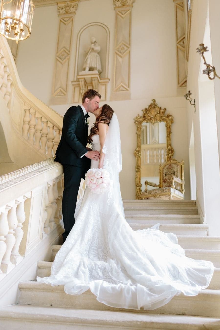 Newlyweds kissing on an ornate gilded staircase, bridal train flowing, at a Paris chateau wedding by SabShots