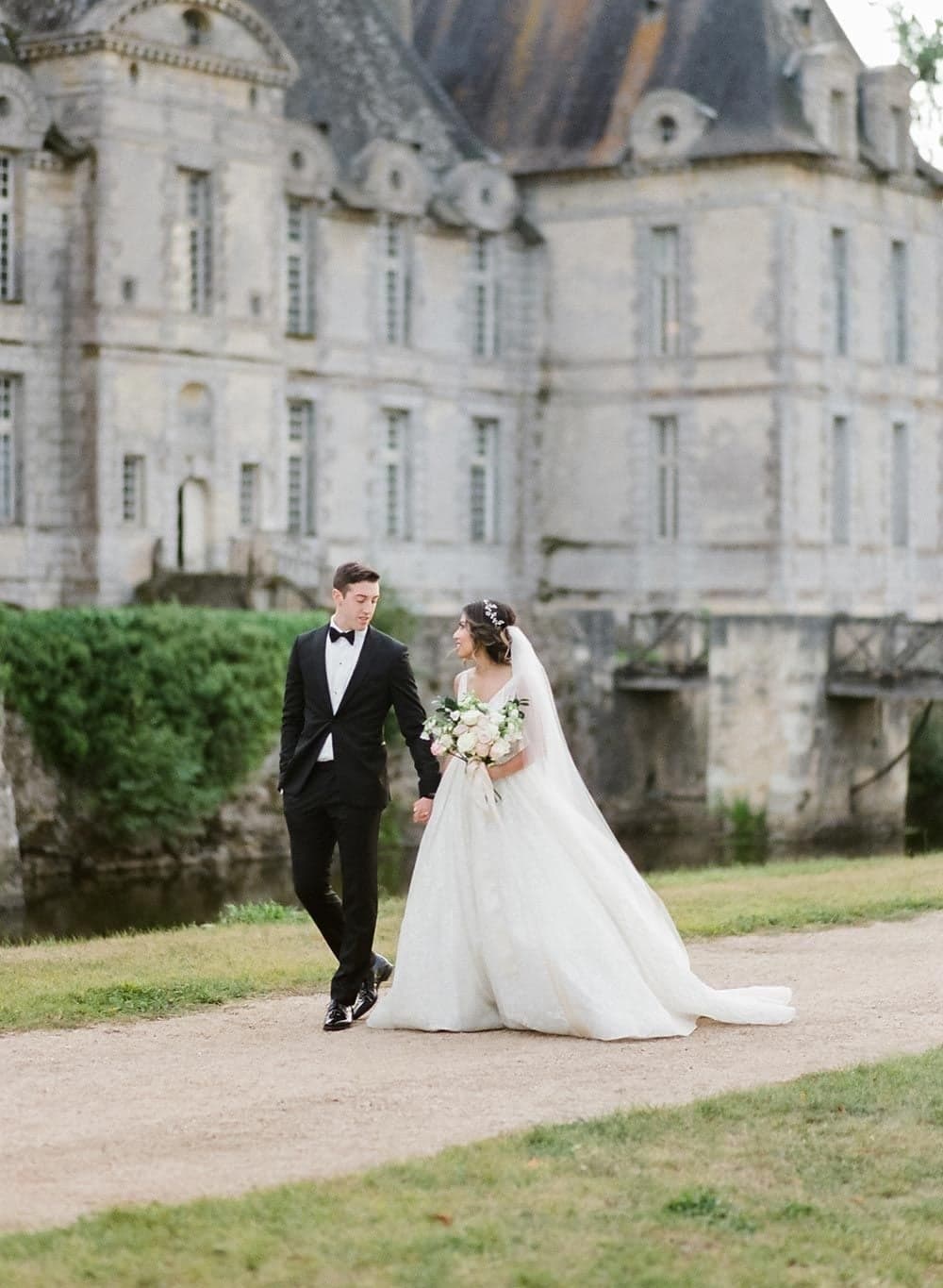 Wedding couple strolling past a grand French chateau facade during their Paris wedding shoot by SabShots