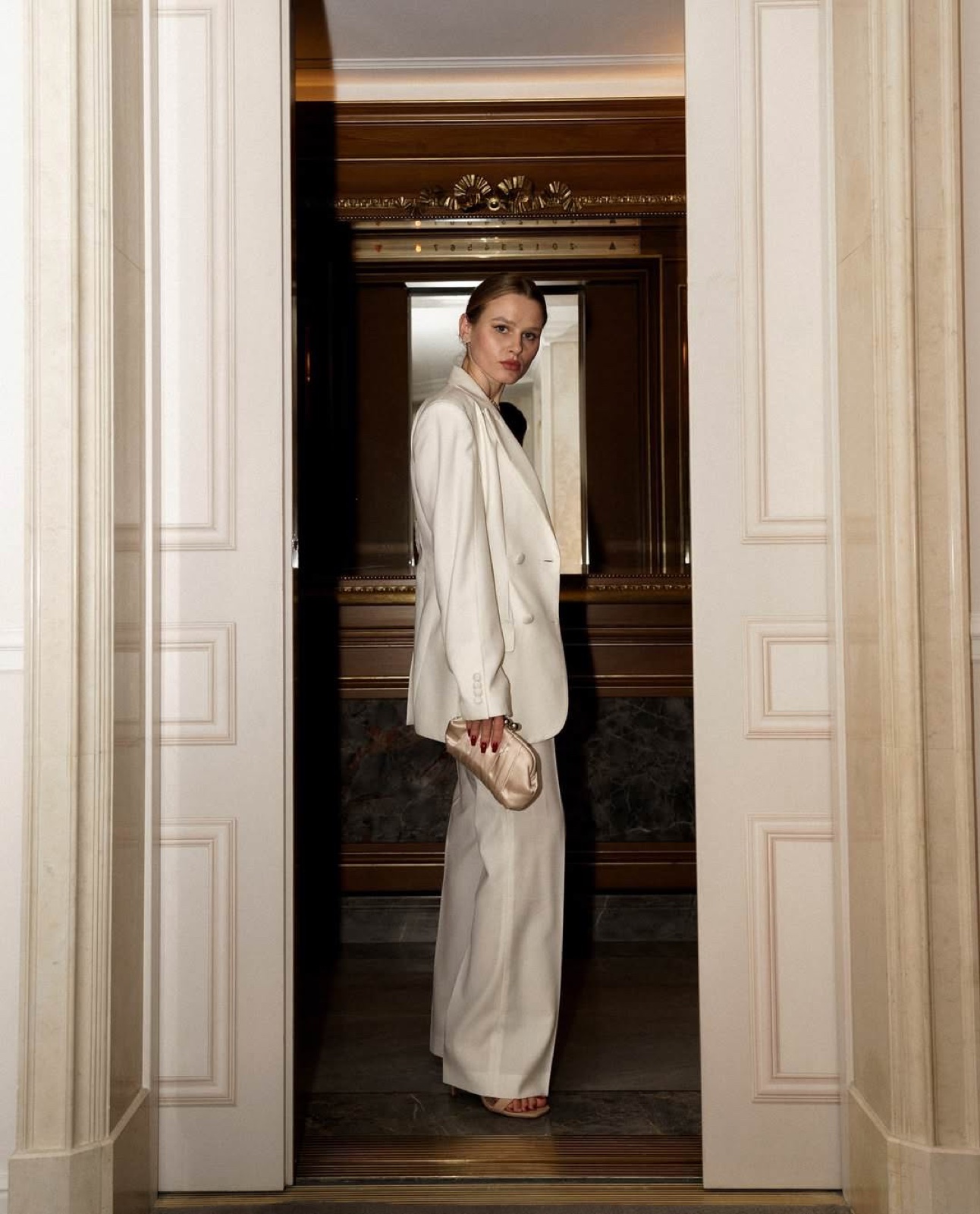 Woman in a cream suit waiting in an ornate Parisian doorway, an outfit prepared for a Paris photo session by SabShots